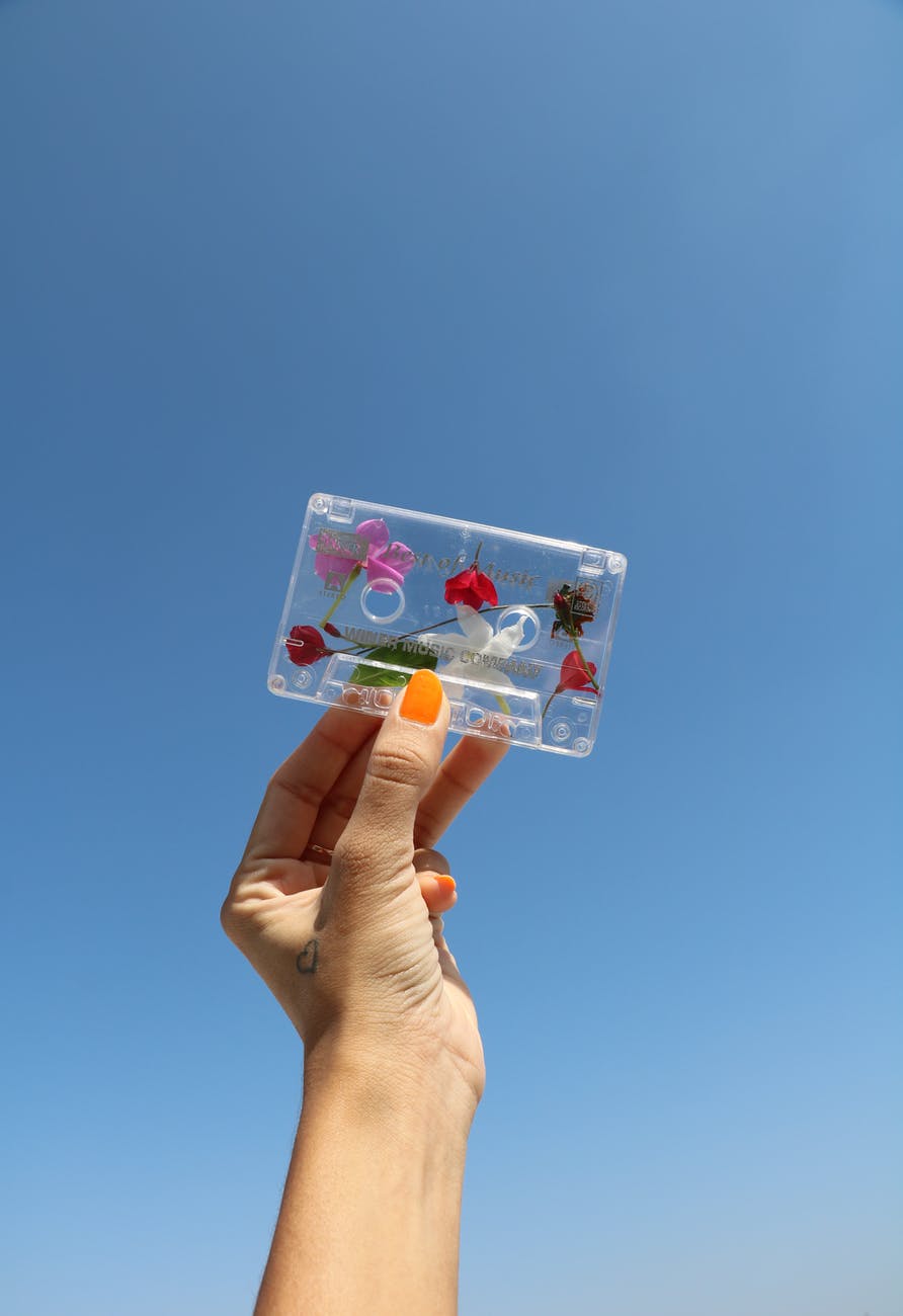 person holding white and pink floral cassette tape